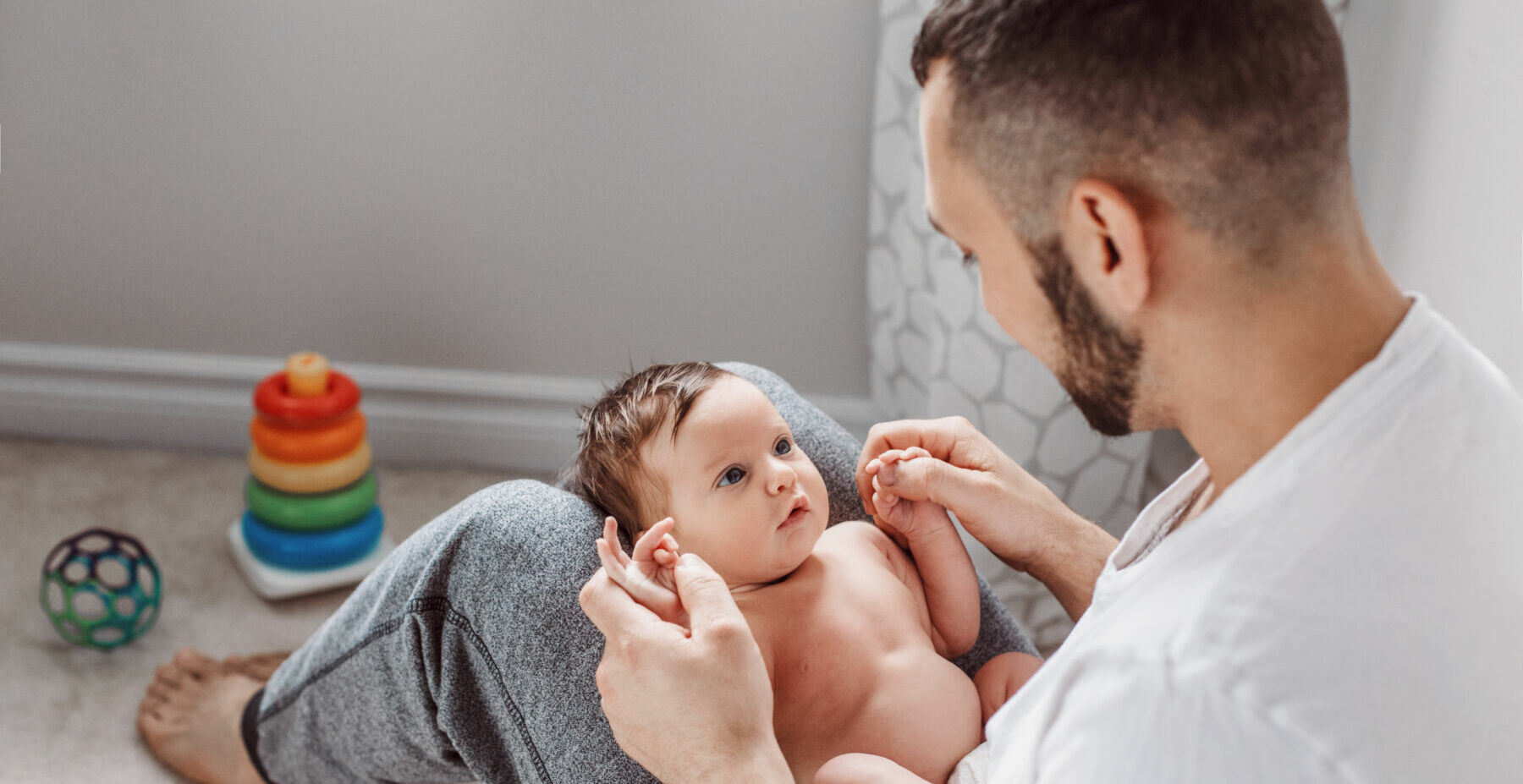 Young Caucasian bearded father holding newborn baby on laps knees. Male man parent rocking talking to child daughter son. Authentic lifestyle documentary moment. Single dad family life.
